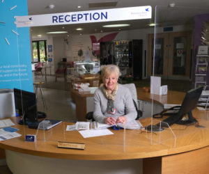 Smiling volunteer receptionist behind a screen at the reception desk