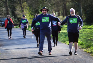 Two men holding hands as they walk the Talk the Walk event route - both are wearing blue and green event t-shirts.