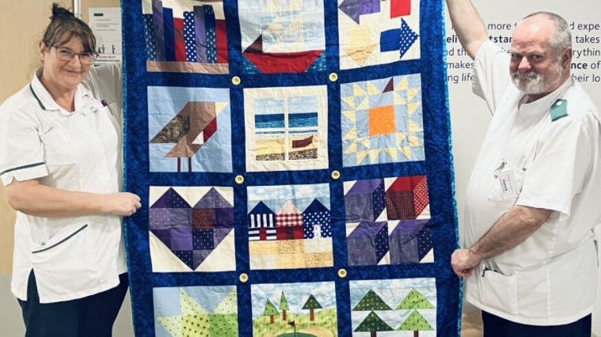 Two nurses holding up a hand made blanket